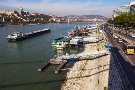 Photo for Budapest, Hungary - February 22, 2015: Boats stationed at Petofi feribot terminal and a barge travelling on Danube river. Buda Castle in the background. - Royalty Free Image