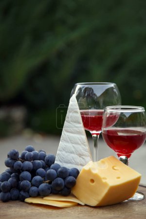 Photo for Composition with a glass of red wine, grapes and cheese. Red natural wine, cheese and a bunch of grapes in a garden in nature. - Royalty Free Image