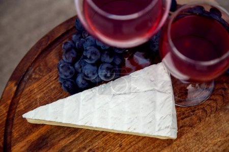Téléchargez les photos : Composition avec un verre de vin rouge, raisins et fromage. Vin rouge naturel, fromage et un bouquet de raisins dans un jardin en pleine nature. - en image libre de droit