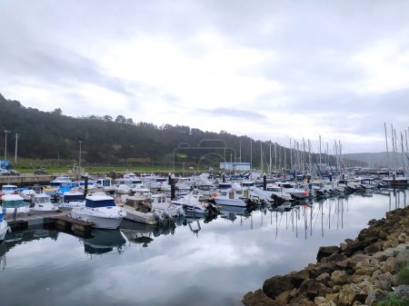 A bustling marina with a multitude of boats, docked and sailing, on a cloudy day.