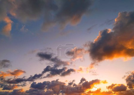 Le soleil se couche, projetant une lueur chaude sur les nuages dans le ciel. Les couleurs vibrantes du coucher de soleil se reflètent dans les nuages, créant une scène dramatique et belle.