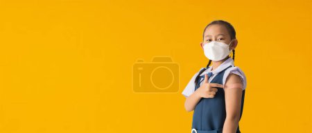 Foto de Back to school banner idea concept, Asian student little girl showing pointing with finger to bandage on her arm shoulder wearing protective mask done with vaccinations - Imagen libre de derechos
