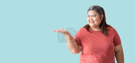 Téléchargez les photos : Fat woman asian happy smiling with hand blank space and showing, isolated on blue background - en image libre de droit