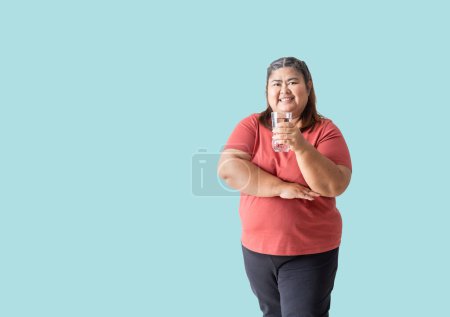 Téléchargez les photos : Fat woman asian happy smiling holding a glass of water, isolated on blue background - en image libre de droit
