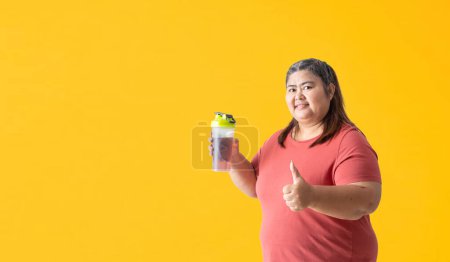 Photo for Fat woman holding a water or supplement bottle and thumbs up, isolated on yellow background. Clipping paths for design work empty free space - Royalty Free Image