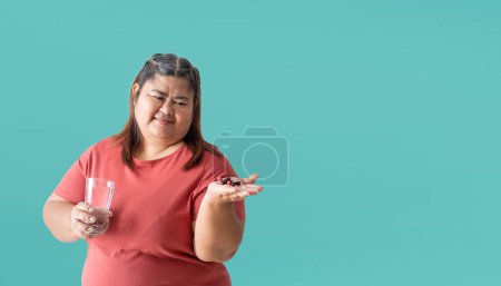 Foto de Fat woman bored hand holding pills  isolated on blue background. Clipping paths for design work empty free space - Imagen libre de derechos