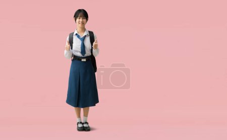 Photo for Full body Asian student girl wearing uniform with smiling giving thumbs up, isolated on pink background with Clipping paths for design work empty free space - Royalty Free Image