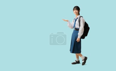 Téléchargez les photos : Full body Asian student girl wearing uniform hold backpack with hand holding open palm up blank space, isolated on blue background with Clipping paths for design work empty free space - en image libre de droit