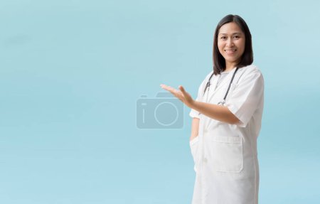 Téléchargez les photos : Smiling asian female doctor medical professional holding something in empty hand, isolated on blue background with Clipping paths for design work empty free space - en image libre de droit
