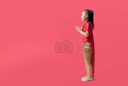 Photo for Asian little girl in Thai national costumes with welcome gesture of hands of Thailand, isolated on red background with Clipping paths for design work empty free space - Royalty Free Image