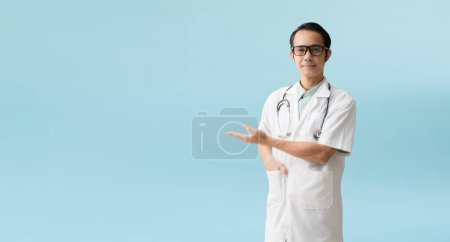 Foto de Asian man doctor medical professional holding something in empty hand, isolated on blue background with Clipping paths for design work empty free space - Imagen libre de derechos