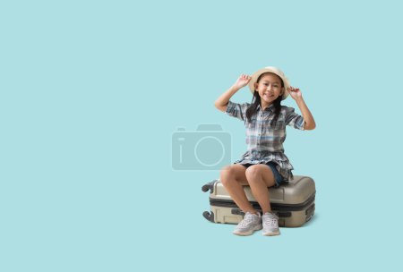Téléchargez les photos : Pretty asian little girl sits on a suitcase adventure vacation travel trip dream concept. Smiling cute little girl isolated on blue background with Clipping paths for design work empty free space - en image libre de droit