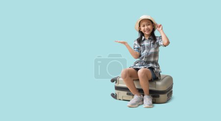 Téléchargez les photos : Pretty asian little girl sits on a suitcase with hand holding open palm up blank space, Adventure vacation travel trip dream concept. isolated on blue background with Clipping paths for design work - en image libre de droit