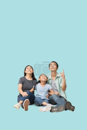 Téléchargez les photos : Happy souriant jeune famille asiatique regardant vers le haut et pointant doigt espace de travail vierge, Famille ont un temps amusant ensemble Corps complet isolé sur fond bleu clair pastel - en image libre de droit