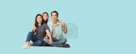 Photo for Happy smiling young asian family sitting on floor and have a fun time together, Full body isolated on pastel plain light blue background - Royalty Free Image