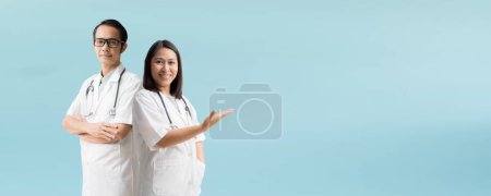 Photo for Medical Services. Asian doctor woman and man, Posing arms crossed with Hand open palm up, isolated on blue background - Royalty Free Image