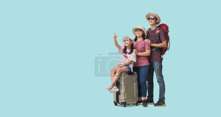 Foto de Family Travel Concept, Full body Felices vacaciones familiares asiáticas, Padre, madre e hija pequeña se sientan en maletas con la mano apuntando listo para el viaje de vacaciones, aislado en pastel liso azul claro - Imagen libre de derechos