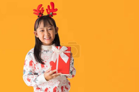 Foto de Alegre niña asiática vistiendo un suéter de Navidad con cuernos de reno, Feliz sonrisa mientras sostiene la caja de regalo de Navidad Feliz Año Nuevo, aislado sobre fondo blanco, Caminos de recorte - Imagen libre de derechos