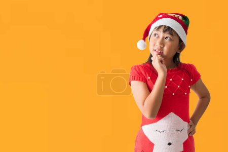 Foto de Feliz niña asiática sonriente en sombrero de Santa Claus con un traje rojo de Navidad, mirando posando sorpresa de pie, aislado sobre fondo amarillo - Imagen libre de derechos