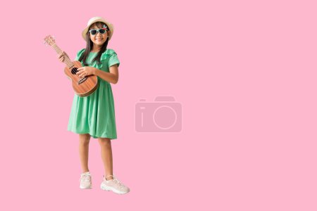 Happy smiling asian little girl were hat and sunglasses playing Ukulele exuding fun. Full body isolated on pink  background