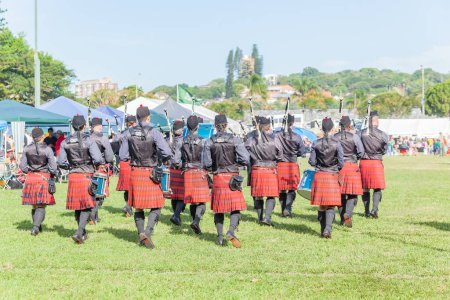 Téléchargez les photos : Scottish band musicians marching performance at highland games a rear view photograph outdoor field venue summer blue sky day. - en image libre de droit