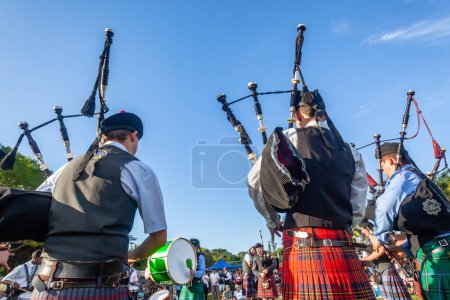Téléchargez les photos : Scottish band musicians bagpipes performance at highland games a rear view photograph outdoor field venue summer blue sky day. - en image libre de droit