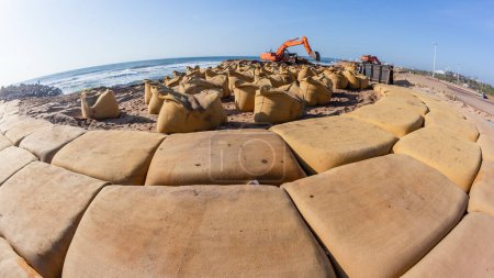 Construcción a plazos en la costa de la playa de grandes bolsas de arena de lona colocadas como una barrera de protección contra las tormentas de agua de mar y mareas. .