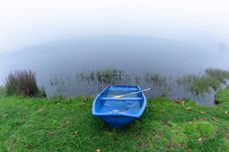 Blue Paddle Boat along waters edge of  dam covered with cloud mist arriving over  with autumn season arriving in countryside holiday landscape.