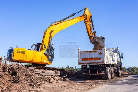 Construction Excavator machine dumping earth into truck industrial earthworks landscaping on highway embankment layout of highway improvements.