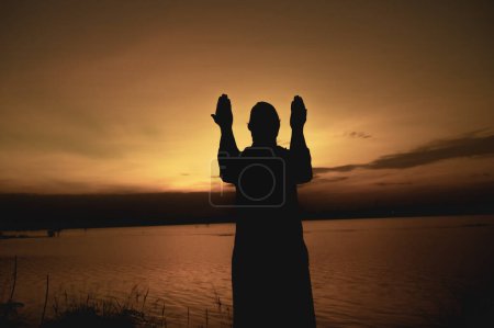 Téléchargez les photos : Silhouette Jeune homme musulman asiatique priant au coucher du soleil, concept du festival Ramadan - en image libre de droit