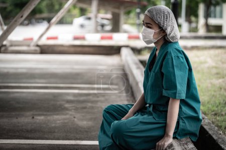 Photo for Tired depressed female asian scrub nurse wears face mask blue uniform sits on hospital floor,Young woman doctor stressed from hard work - Royalty Free Image