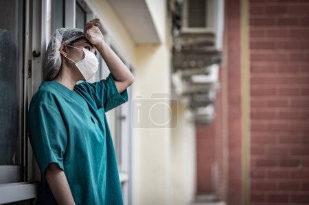 Téléchargez les photos : Fatigué déprimé femme asiatique gommage infirmière porte masque visage uniforme bleu se trouve sur le sol de l'hôpital, Jeune femme médecin stressé par le travail acharné - en image libre de droit