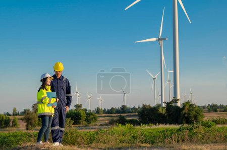 Photo for Two engineers working and holding the report at wind turbine farm Power Generator Station on mountain,Thailand people,Technician man and woman discuss about work - Royalty Free Image