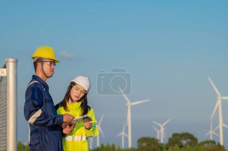 Foto de Dos ingenieros que trabajan y sostienen el informe en la estación de generación de energía de la granja de aerogeneradores en la montaña, Tailandia personas, Técnico hombre y mujer discutir sobre el trabajo - Imagen libre de derechos