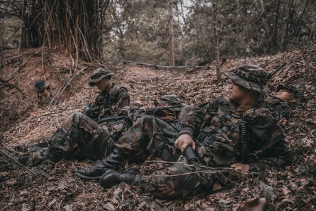 Foto de Equipo de soldado del ejército con ametralladora moviéndose en el bosque, soldado de la milicia tailandesa en uniformes de combate en el bosque, vagar por la patrulla inclinada en la selva tropical. - Imagen libre de derechos