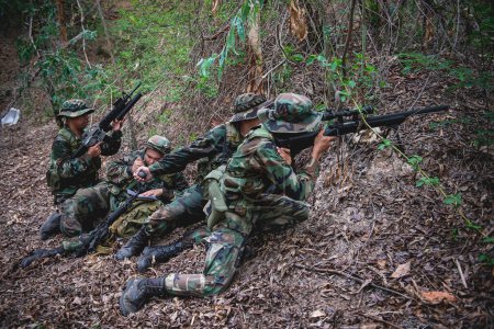 Foto de Equipo de soldado del ejército con ametralladora moviéndose en el bosque, soldado de la milicia tailandesa en uniformes de combate en el bosque, vagar por la patrulla inclinada en la selva tropical. - Imagen libre de derechos