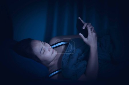 Foto de Mujer asiática jugar smartphone en la cama por la noche, Tailandia personas - Imagen libre de derechos