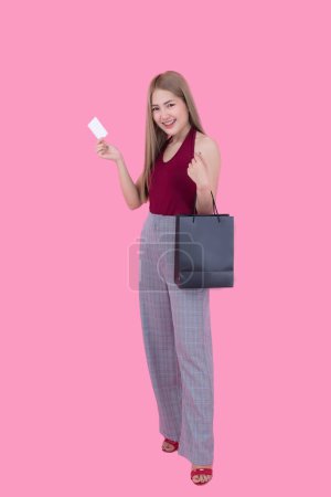 Foto de Hermosa mujer asiática con bolsa de compras y tarjeta de crédito en la mano sobre fondo rosa, Tailandia personas está utilizando una tarjeta de crédito y disfruta de compras - Imagen libre de derechos