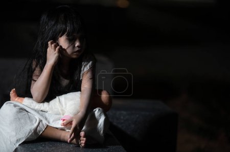 Foto de Sad child ghost at night,Halloween  Festival concept,Friday 13th,Horror movie scene,A girl with doll - Imagen libre de derechos