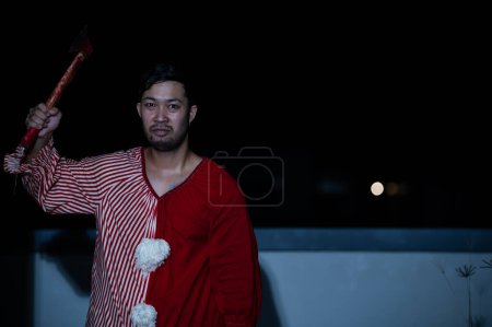 Foto de Hombre guapo asiático usar vestido de payaso con arma en la escena de la noche, concepto de festival de Halloween, Horror aterrador foto de un asesino en tela naranja, Caractor payaso malvado - Imagen libre de derechos