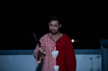 Téléchargez les photos : Asiatique bel homme porter robe de clown avec arme sur la scène de nuit, concept de festival d'Halloween, Horreur photo effrayante d'un tueur en tissu orange, clown maléfique Xotor - en image libre de droit