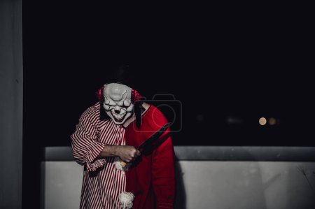 Foto de Hombre guapo asiático usar máscara de payaso con arma en la escena de la noche, concepto de festival de Halloween, Horror aterrador foto de un asesino en tela naranja, Caractor payaso malvado - Imagen libre de derechos