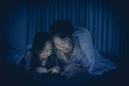 Téléchargez les photos : Dad and daughter sleep on the bed in bedroom,Watch cartoon with phone,Father day concept,Single dad,listen tale before sleep - en image libre de droit