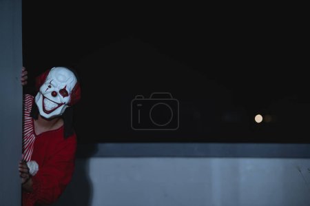 Téléchargez les photos : Asiatique bel homme porter un masque de clown avec une arme sur la scène de nuit, concept de festival Halloween, Horreur photo effrayante d'un tueur en tissu orange, clown maléfique Xotor - en image libre de droit
