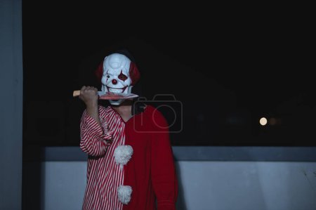 Foto de Hombre guapo asiático usar máscara de payaso con arma en la escena de la noche, concepto de festival de Halloween, Horror aterrador foto de un asesino en tela naranja, Caractor payaso malvado - Imagen libre de derechos