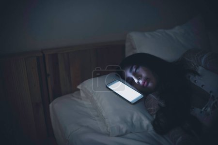 Mujer asiática jugando en el teléfono inteligente en la cama por la noche, Tailandia personas, adicto a las redes sociales
