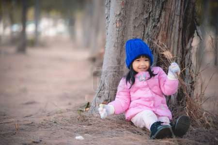 Téléchargez les photos : Portrait de mignonne petite fille asiatique porter des vêtements d'hiver à la forêt du parc, les gens de Thaïlande posent pour prendre une photo, Happy time - en image libre de droit