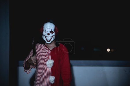 Photo for Asian handsome man wear clown mask with weapon at the night scene,Halloween festival concept,Horror scary photo of a killer in orange cloth,Evil clown charactor - Royalty Free Image