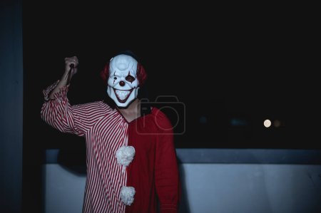 Téléchargez les photos : Asiatique bel homme porter un masque de clown avec une arme sur la scène de nuit, concept de festival Halloween, Horreur photo effrayante d'un tueur en tissu orange, clown maléfique Xotor - en image libre de droit