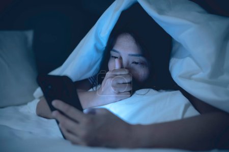 Foto de Mujer asiática jugando en el teléfono inteligente en la cama por la noche, Tailandia personas, adicto a las redes sociales - Imagen libre de derechos